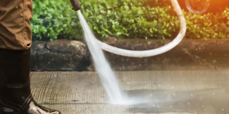 Worker pressure washing a concrete pathway beside hedges.